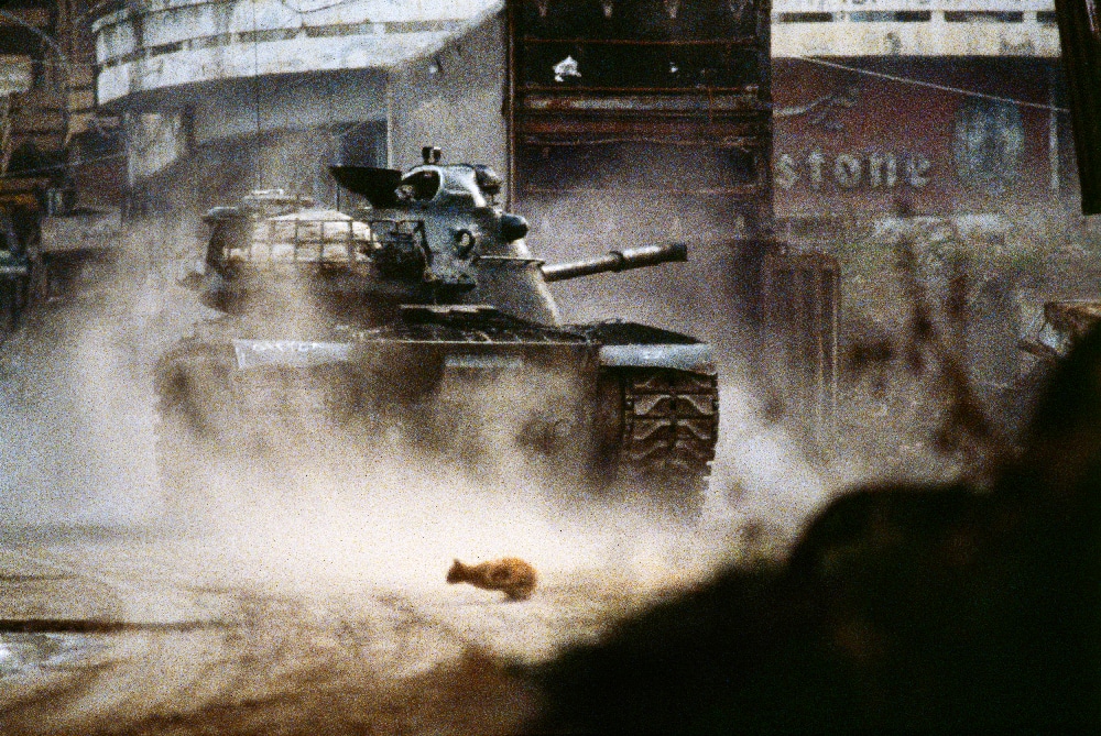 Liban, 1984. Un tank de l’armée libanaise chrétienne tire sur les milices musulmanes dans le centre-ville de Beyrouth. Un chat de religion indéterminée fuit les combats © Patrick Chauvel