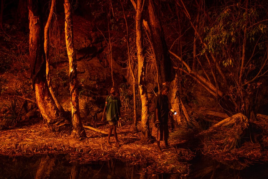 Stacey Lee (11, left) sets the bark of trees alight to produce a natural light source to help hunt for file snakes (Acrochordus arafurae), in Djulkar, Arnhem Land, Australia, on 22 July 2021. © Matthew Abbott / Panos Pictures for National Geographic