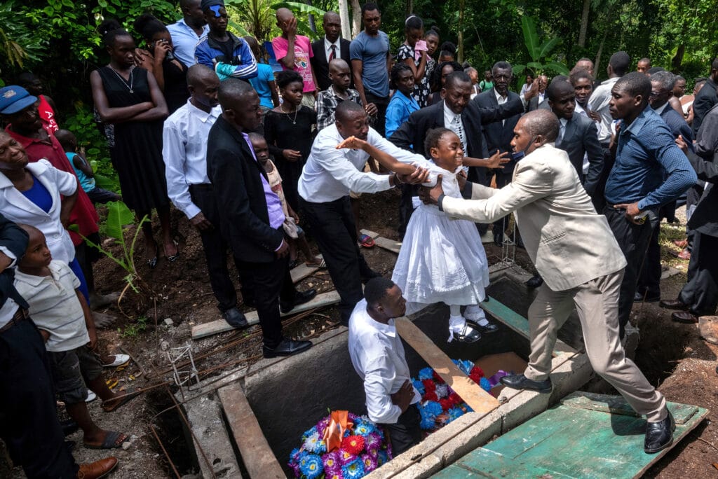 Grandchildren are passed over the gravesite in a poignant tradition as a family holds a village funeral for Marie Herese Atineus who died when her home collapsed during a massive earthquake as Haitians cope with the aftermath in Maniche, Haiti on Saturday August 21, 2021 © Carol Guzy