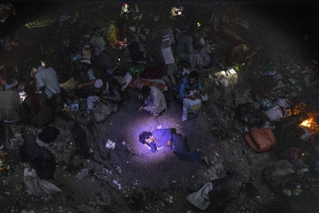 A policeman shines a flashlight on a man suspected of overdosing as drug addicts are seen smoking heroin and methamphetamine in an area where hundreds of users shelter live in squalid conditions at Pul-e-Sukhta, under a bridge in western Kabul © Paula Bronstein