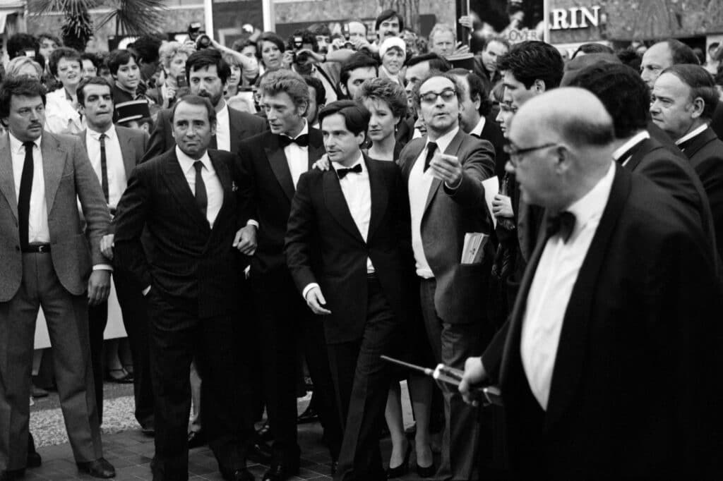 French cast of the film "Detective", Claude Brasseur (4th L), Johnny Hallyday (5th L), Jean-Pierre Léaud (C), Nathalie Baye (behind), film director Jean-Luc Godard (3rd R) and Stéphane Ferrara, arrive at the 38th International Film Festival in Cannes. © Dominique FAGET and Ralph GATTI / AFP