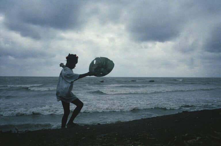 Daily life in this seaside town that was once a tourist haven, the only place in Haiti that's still green with vegetation, but is filthy and poor, with no plumbing or electricity in a majority of the homes. Small girl dumps out the family garbage into the sea. Jeremie, Haiti, January, 2006 © Jane Evelyn Atwood