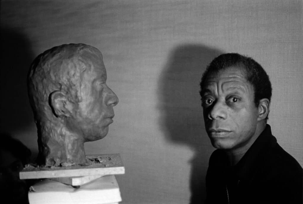 James Baldwin with the bust of his head by American artist, Lawrence Wolhandler - in his hotel room, rue des Grands Augustins, Paris, France. 1975 © Jane Evelyn Atwood