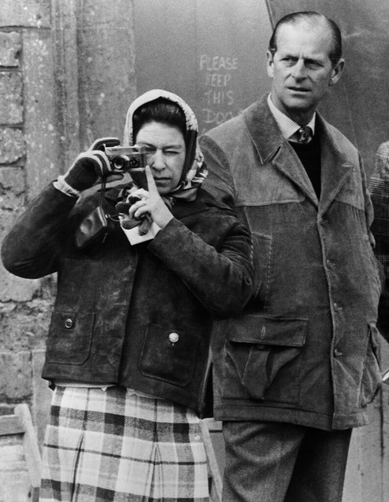 La reine Elizabeth II, tenant son appareil photo Rollei, prend des photos de son cheval "Columbus" avant de participer aux Badminton Horse Trials, le 26 avril 1974, sous le regard du prince Philip, duc d'Édimbourg. © AFP