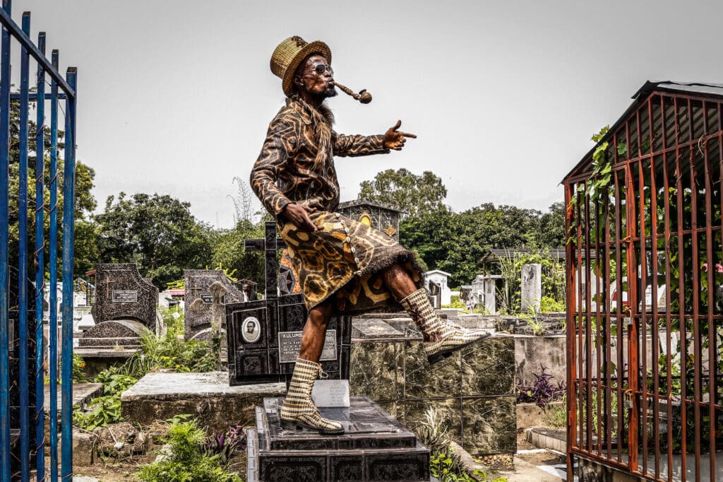 Sapeur Koko Lingwala poses atop a grave in the cemetery in the Gombe neighborhood of Kinshasa on February 10 to commemorate the anniversary of the death of Stervos Niarcos, who died 26 years ago in Paris and is revered as the founder of modern sapeurism, the Society of Tastemakers and Elegant People (or Societe des Ambianceurs et des Personnes Elegantes in the original French, or SAPE for short). © Justin Makangara / Fondation Carmignac