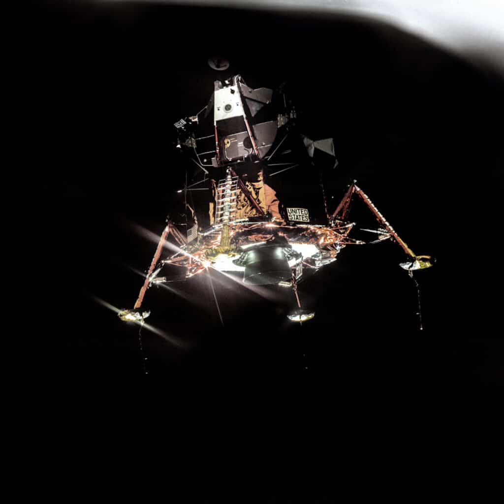20 juillet 1969, Hasselblad 70 mm. Objectif 80mm F/2,8 par Michael Collins, Réf NASA: AS11-44-6576. Collins : « OK, voilà. Magnifique ! » CapCom Duke (astronaute habilité à communiquer avec un équipage pendant une mission) : « Comment ça se présente, Neil ? » Armstrong : « L’aigle a des ailes ! » Armstrong prend les commandes pour permettre une inspection visuelle du module lunaire, avant la mise à feu d’insertion dans l’orbite de descente. Notez l’absence d’une des sondes de contact, au pied de l’échelle. Elle a été retirée, car Armstrong craignait qu’elle ne se replie vers le haut et ne présente un danger lors de la descente par l’échelle. Armstrong est tout juste visible, à la barre, dans le hublot triangulaire gauche du module lunaire. © NASA_JSC_ASU_Andy Saunders
