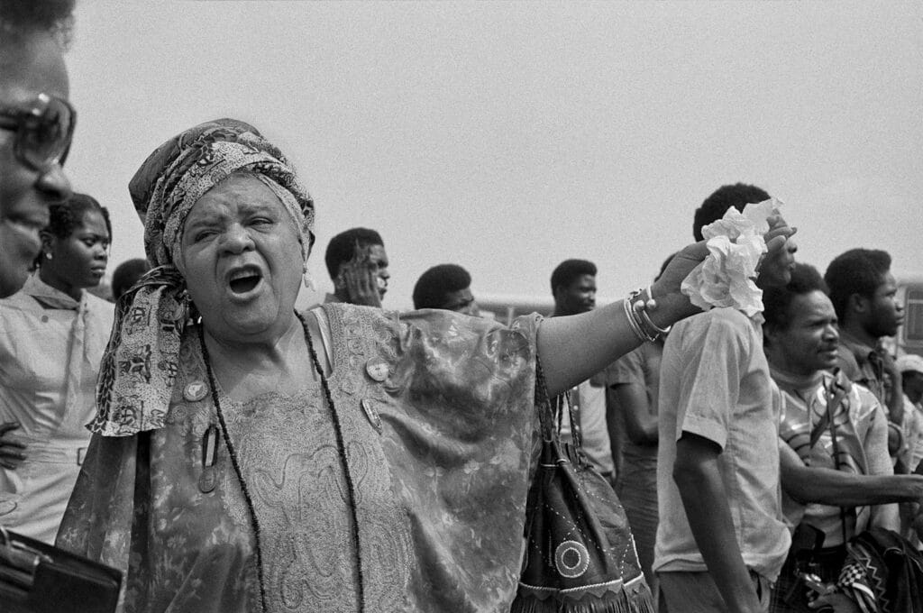 Distinguished Elder Queen Mother Audley A. Moore at Lagos airport. In the background are artists Charlotte Richardson-Ka ( L ) and Wadsworth Jarrell ( R ), 1977 © Marilyn Nance / Artists Rights Society (ARS), New York