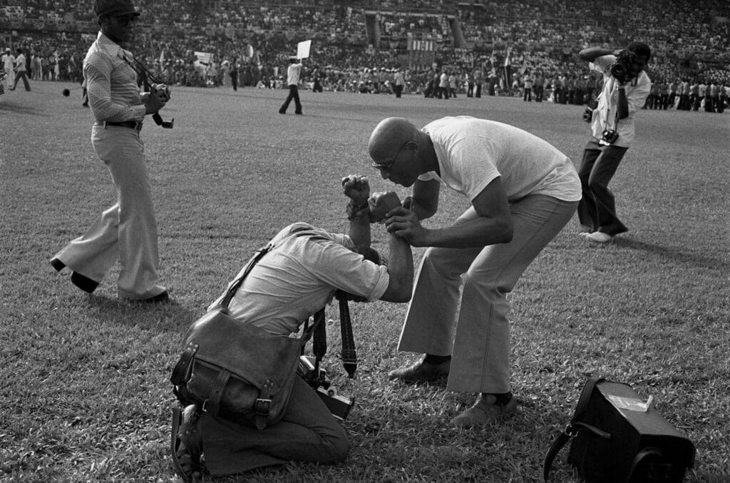 Cérémonie d'ouverture du FESTAC '77 : le photographe Ted Pontiflet salue son ami l'artiste Abdul Rahman sur le terrain du Stade National., 1977 © Marilyn Nance / Artists Rights Society (ARS), New York