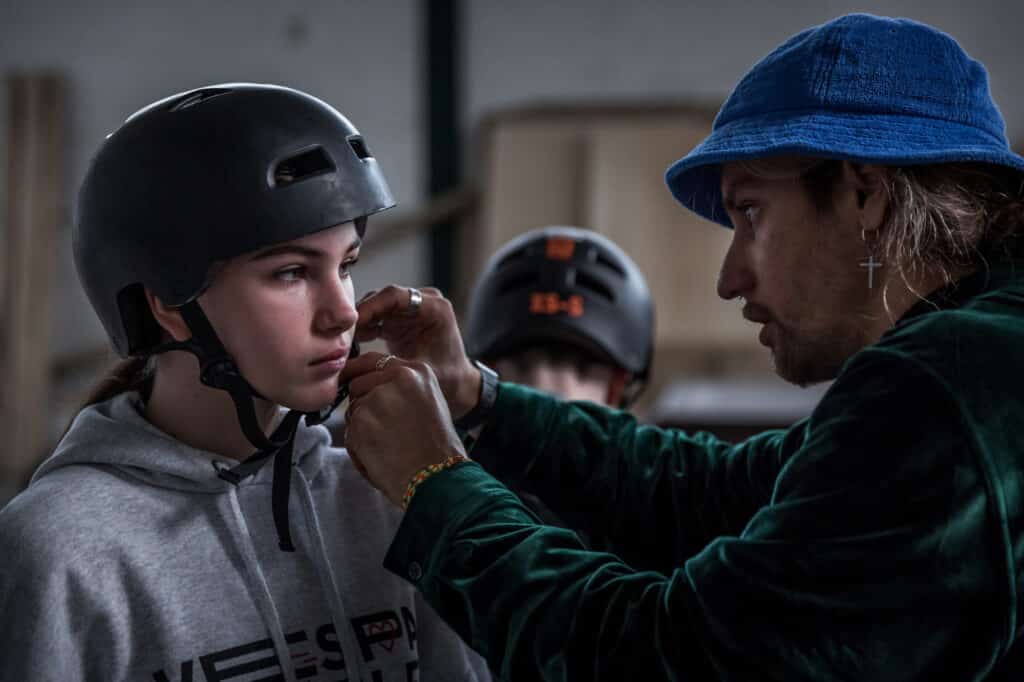 Yurii helps Karina, 14 from Odessa, to fasten her helmet. Thanks to a partnership with European online skateshop Blue Tomato who wished to support the positive initiative of giving skateboarding courses to the refugees, Gleis D Skate Halle’staff received from the company numerous free skateboards and protective gears such as helmets, elbow and knee pads for the rookies. Hanover, Germany. April 14th, 2022. © Thomas Girondel