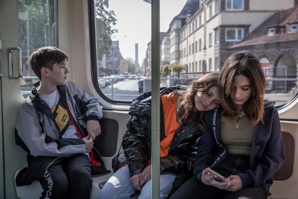 Sur le chemin du retour au camp de réfugiés de Messe, tandis qu'Arthur regarde par la fenêtre du tramway, Erika se repose sur l'épaule de Karina en regardant son téléphone portable. Hanovre, Allemagne, 27 avril 2022. © Thomas Girondel