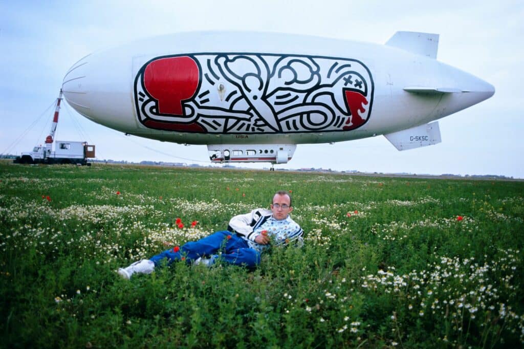 Keith Haring with blimp in France, 1989. Photo: Tseng Kwong Chi © Muna Tseng Dance Projects Inc, Art: © Keith Haring Foundation, courtesy of Yancey Richardson Gallery