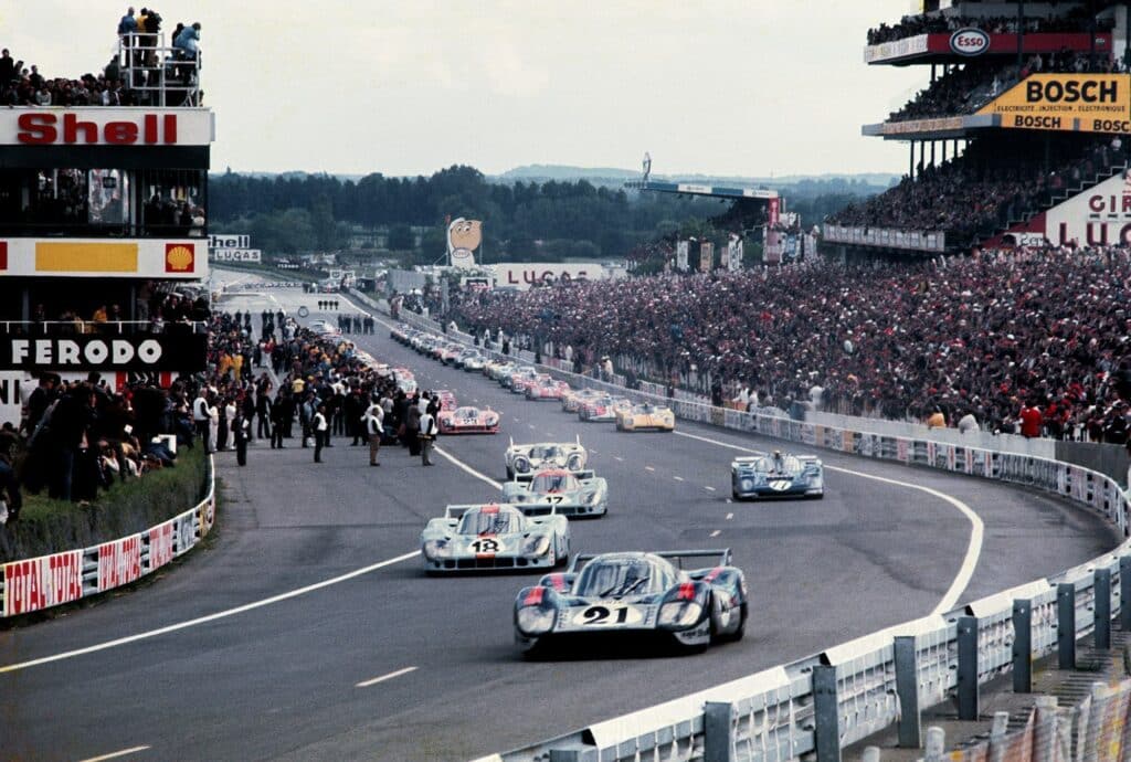 The Porsche’s legendary 917s lead the charge in 1971 as fans cram into the stands and members of the press and drivers’ teams watch from the sideline. © Joe Honda / Le Mans Collection