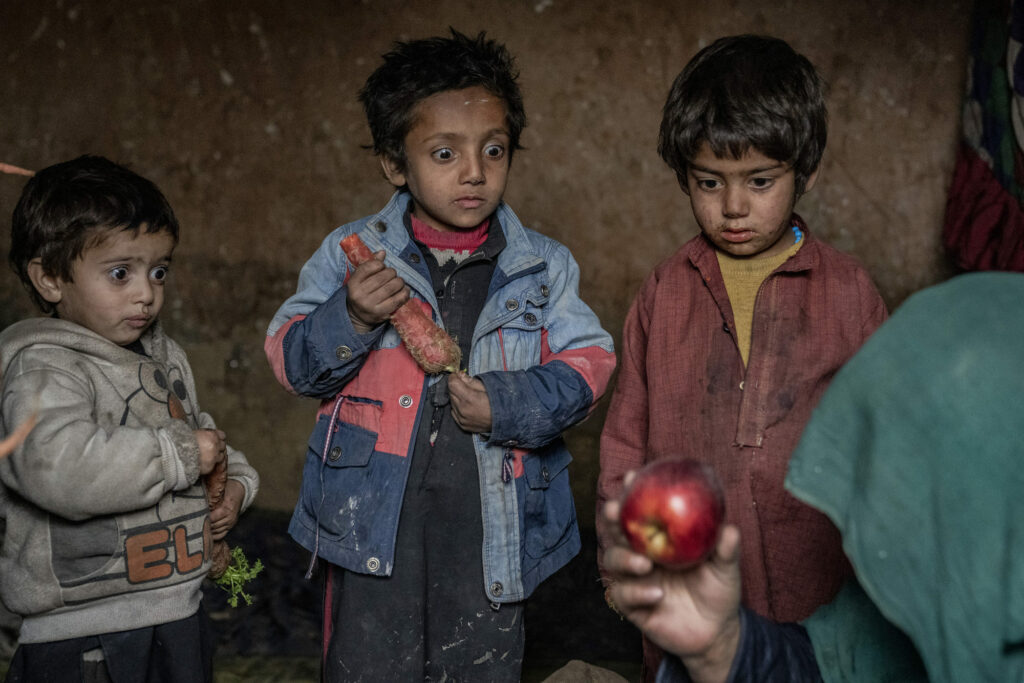Three Afghan internally displaced children look with surprise at an apple that their mother brought home, in the outskirts of Kabul, Afghanistan, Thursday, Feb 2, 2023.
