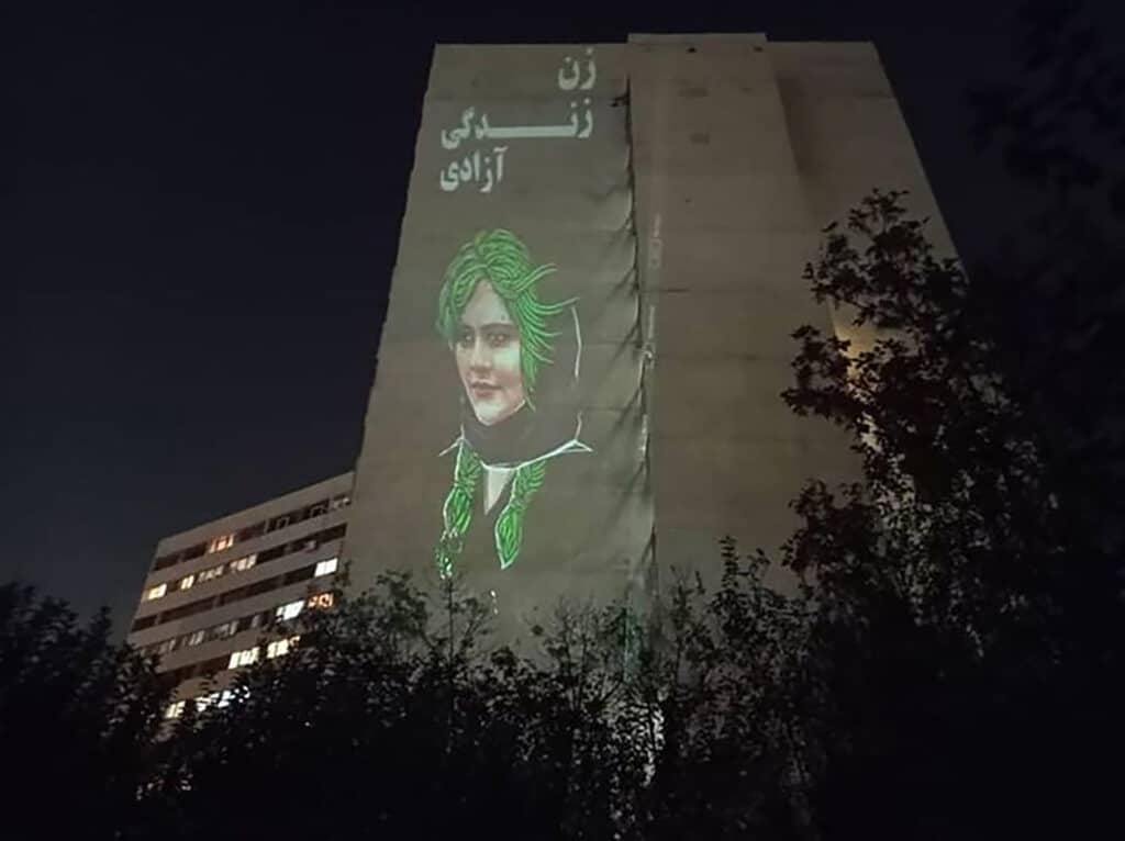 Le visage de Mahsa Amini projeté sur la façade d’un immeuble du quartier d’Ekbatan, accompagné du slogan « Femme, vie, liberté ». Téhéran, 25 octobre 2022. Photographe anonyme “Woman, Life, Freedom!” and the portrait of Mahsa Amini. Ekbatan, Tehran, October 25, 2022. Anonymous Photo libre de droit uniquement dans le cadre de la promotion de la 35e édition du Festival International du Photojournalisme "Visa pour l'Image - Perpignan" 2023 au format 1/4 de page maximum. Résolution maximale pour publication multimédia : 72 dpi Mention du copyright obligatoire. Cette image ne pourra plus être utilisée en libre de droit après le 31 décembre 2023. The photos provided here are copyright but may be used royalty-free for press presentation and promotion of the 35th International Festival of Photojournalism Visa pour l'Image - Perpignan 2023. Maximum size printed: quarter page Maximum resolution for online publication: 72 dpi Copyright and photo credits (listed with captions) must be printed. This photo can no longer be used royalty-free after December 31, 2023.