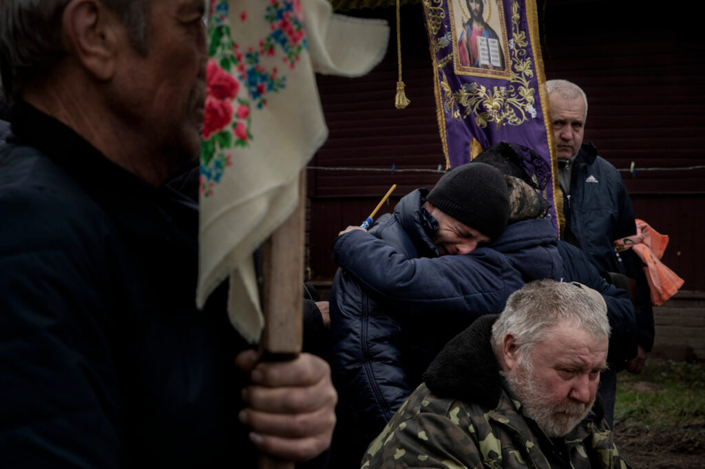Mykola and his sister Irina cry and hug each other, as their father sits, during the funerals of two brothers Dmytro, 36-years-old and Yevheniy, 30-years-old, who torutred and killed by the Russians, in Dovzhyk, Ukraine, on Thu. April 21, 2022. The three brothers Kulichenko were first detained in their house by the Russians, after someone denounced them as being a veteran of the Eastern War front and an ex policemen. They were then detained ni an other village and tortured for two days. The Russians brought them to a distant location, made them dig their own graves and shot them in the back of the head. Mykola survived as the bullet only went through his ear, and managed to walk 40-45 kilometers back home.
