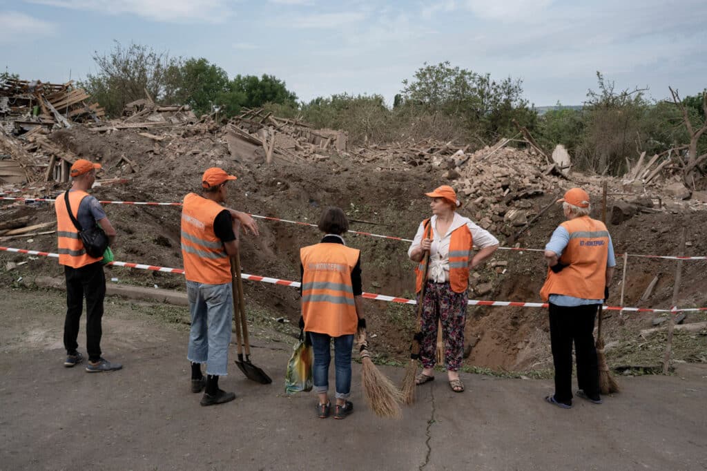 Des gens prennent une pause après avoir nettoyé le principal des déchets laissés sur la route après une frappe entre 2h et 3h du matin, à Droujkivka, Ukraine, le 5 juin 2022.