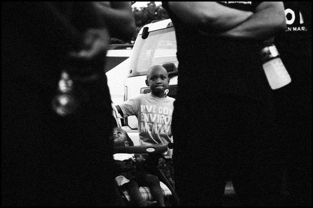 A young boy peers out from behind marchers. In response to the spike in homicides in 2013, Baltimore City Councilman Brandon Scott and activist Munir Bahar organized the 300 Man March, which encouraged men of all ages to walk at night through some of Baltimore's most violent neighborhoods. Neighbors came out fo their houses to cheer the marchers on as they walked through Baltimore's BelAir-Edison neighborhood.